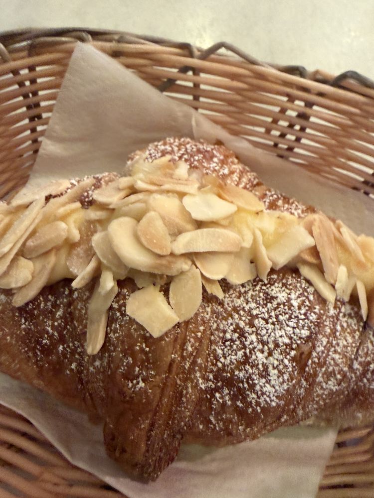 An almond croissant dusted with icing sugar in a wicker basket